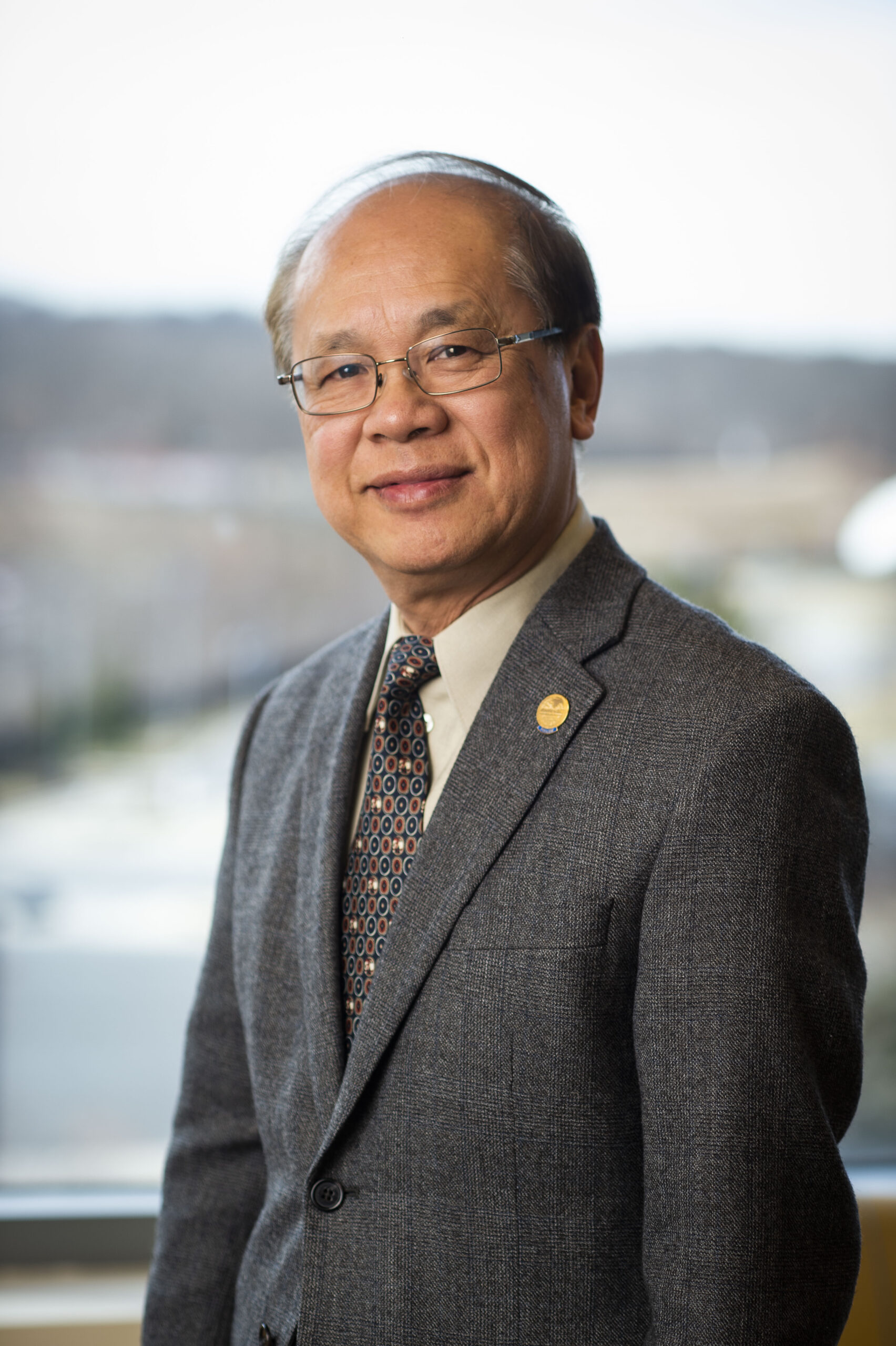 Dr. Lau, wearing a smart suit, smiles to the camera