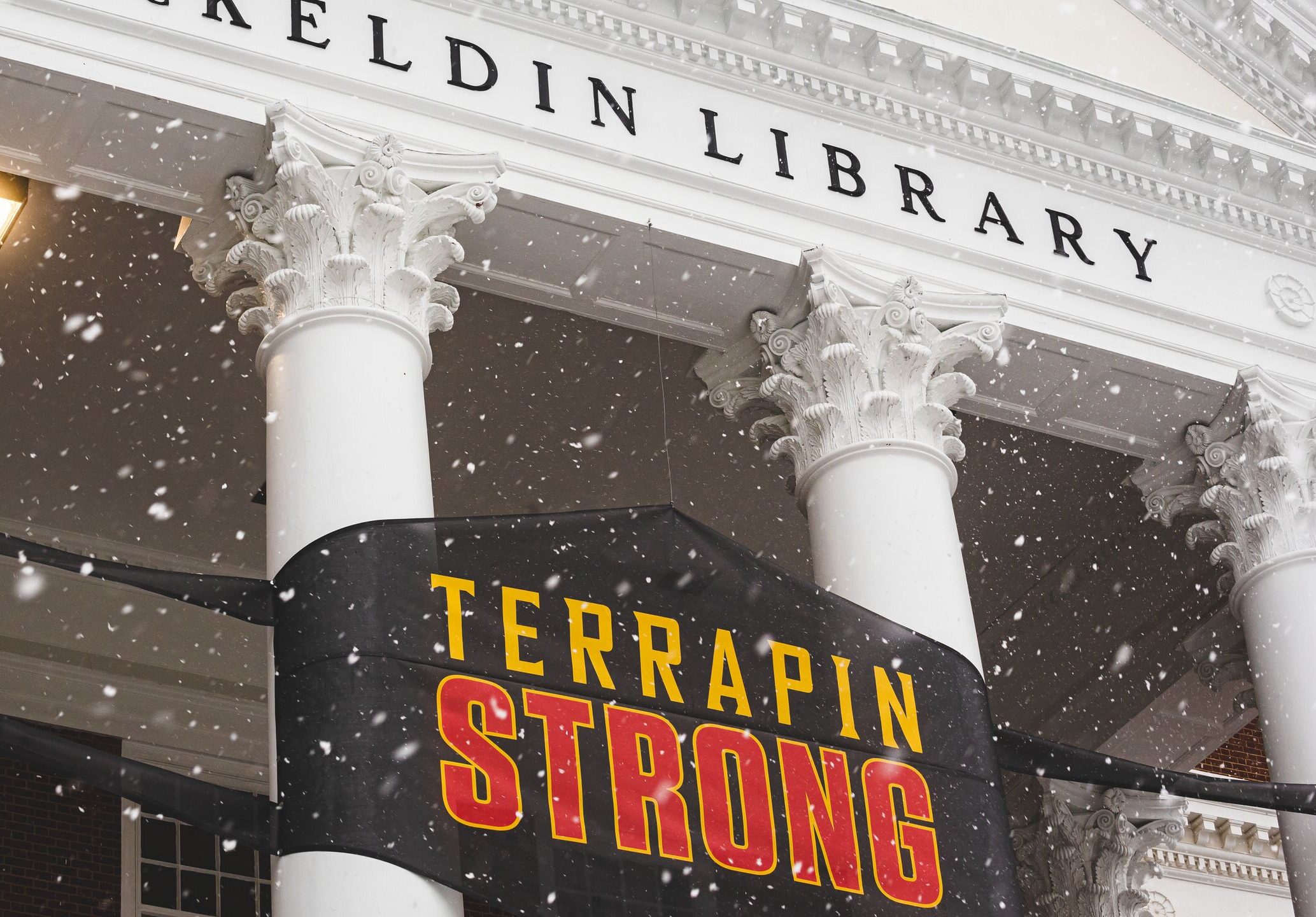 A snowy McKeldin Library with a sign that looks like a face mask that says "Terrapin Strong"