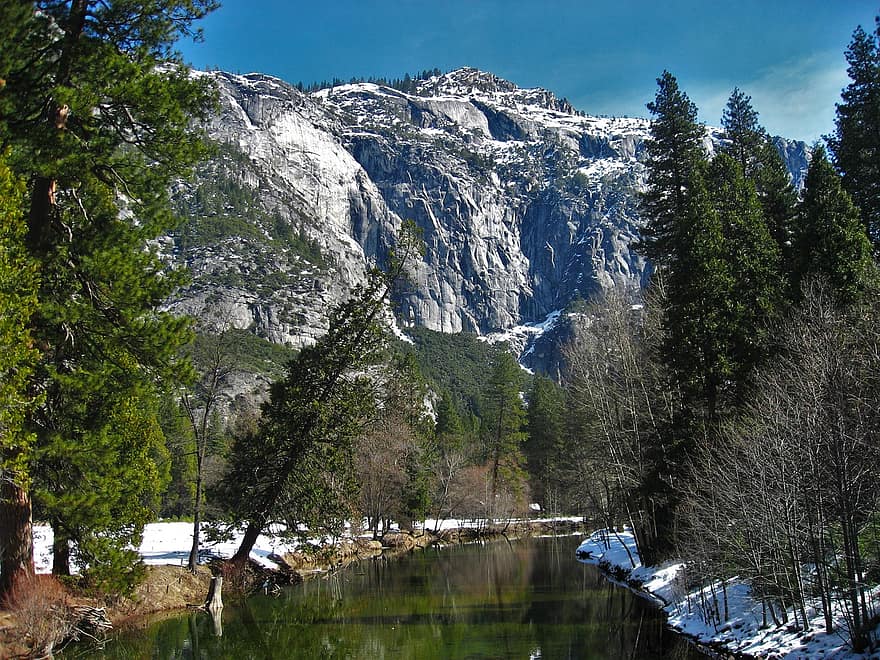 A snowy Yosemite mountain behind a lake, also surrounded by snow